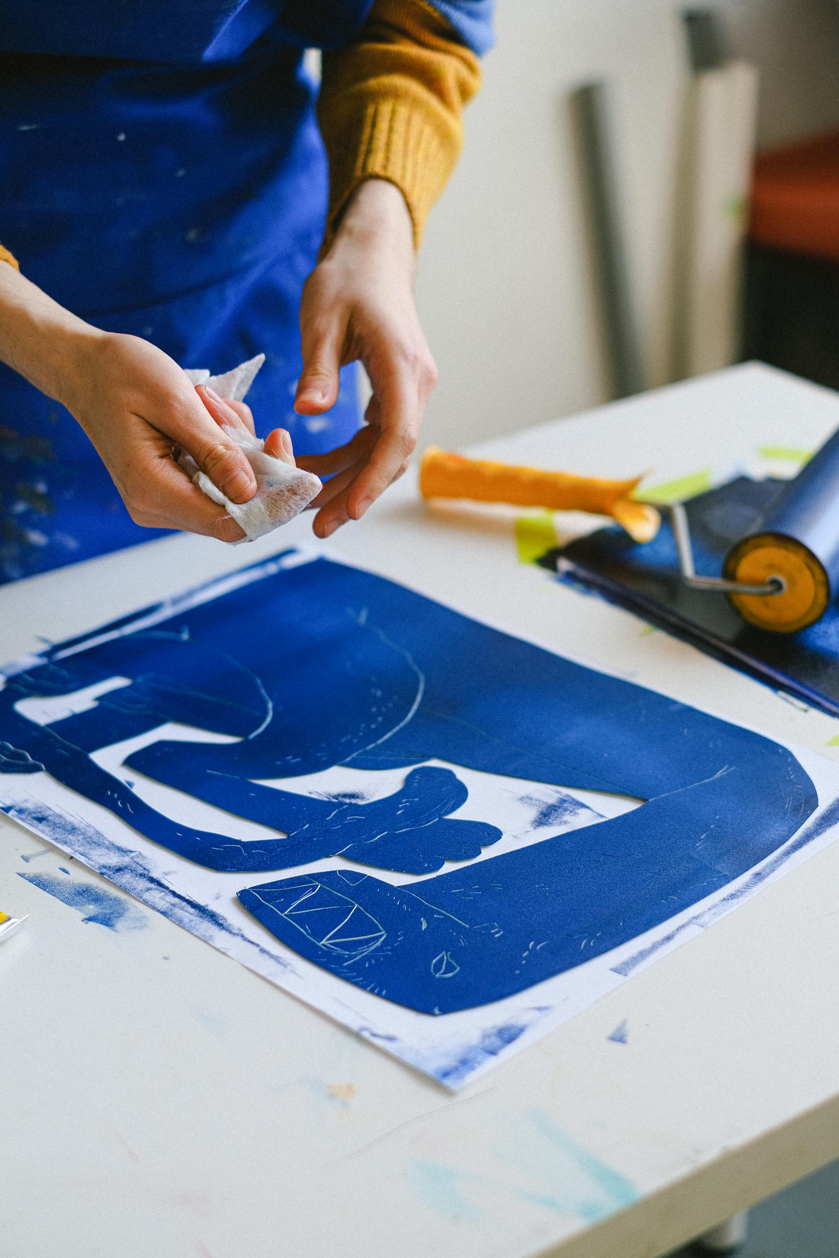 Unrecognizable female artist making stencil for creating etching picture on table in craft shop